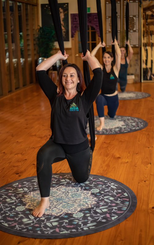 Misty is doing an aerial yoga lunge, with soft focus people lunging in the background