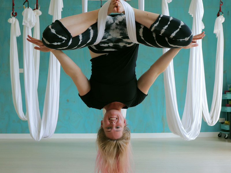 Jo is in an aerial yoga inversion with a blue wall in the background